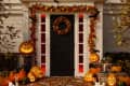 Halloween-themed porch with carved pumpkins, autumn leaf garland, and candles around a black door.