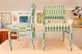 Two striped chairs in blue and green fabric, displayed on a wooden table with art and decor in the background.