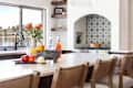 Modern kitchen with a large island, colorful fruits, decorative vase, and patterned backsplash.