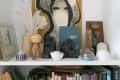 Shelf with eclectic decor including sculptures, feathers in a vase, framed art, and various small objects.
