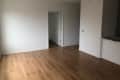 Empty room with light wood flooring, white walls, and a doorway leading to another room.