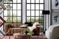 Modern living room with brown leather sofa, round wooden coffee table, and large windows overlooking greenery.