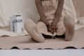Person in beige overalls sitting with crossed legs, showing socks labeled "BACKDROP," next to a paint can.