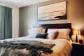 Cozy bedroom with a dark wood headboard, neutral bedding, abstract wall art, and bedside lamps.