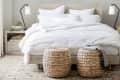 Cozy bedroom with a white bed, wicker stools, bedside tables, lamps, and a patterned rug.