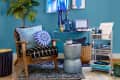 Cozy living room with a wooden chair, blue cushions, patterned rug, and a record player on a teal wall.