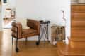 Brown leather chair with a sheepskin throw, black side table, and wicker basket by wooden stairs.
