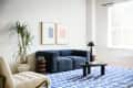 Living room with blue sofa, white walls, art over sofa, natural color armchair, Marimekko/West Elm collab blue and white patterned rug
