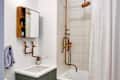Bathroom with copper pipe shower, white curtain, green vanity, and wall-mounted mirror cabinet