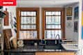 Kitchen sink area with two windows, wooden cutting boards, knives on display, and decorative wall art.