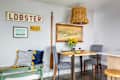 Cozy dining area with a wooden table, gray chairs, floral centerpiece, and wall decor including a lobster sign and painting.