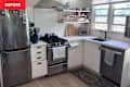 Modern kitchen with stainless steel appliances, white cabinets, open shelving, and a patterned rug.