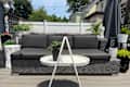 Outdoor seating area featuring a dark gray sectional sofa, a white round table, and various potted plants.