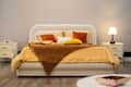 Cozy bedroom featuring a plush bed with yellow and orange pillows, a brown throw blanket, and a bedside lamp.
