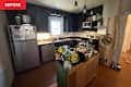 Cluttered kitchen with dark cabinets, stainless steel appliances, and a wooden island filled with plants and kitchen items.