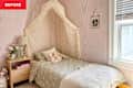 Cozy bedroom with a bed draped in a canopy, soft bedding, stuffed animals, and a nightstand with a lamp and flowers.