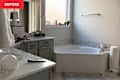 Bathroom with a corner bathtub, gray cabinetry, a sink, and a window with plants on the sill.
