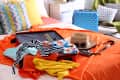 Open suitcase with colorful clothes on bed, straw hat, sunglasses, camera, and blue suitcase in a bright room.