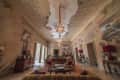 Ornate living room with frescoed walls, chandeliers, armchairs, and decorative tables with red lamps.