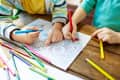 Children coloring intricate floral patterns with colored pencils on a wooden table.
