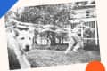 Child running with a large bubble wand, followed by a playful dog on a grassy lawn near a house.