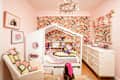 A colorful children's bedroom featuring a house-shaped bed, floral wallpaper, plush toys, and a decorative dresser.