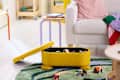 Bright living room with a yellow storage box, colorful toys, a white sofa, and a green rug.