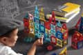Child building with colorful magnetic tiles on a table, surrounded by books and architectural sketches.