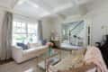 Living room with white sofa, colorful pillows, glass coffee table, and view of staircase with wooden railing.