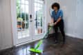 Person mopping a shiny floor in front of glass doors, wearing a blue shirt and black pants.