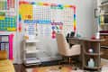 Home classroom with educational posters, beige chair, wooden desk, and floral rug on wooden floor.