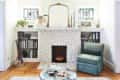 Living room with white brick fireplace, stained glass windows, bookshelves, teal armchair, and decorative plants.