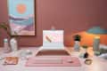 Home office with laptop on stand, pink wall, abstract art, plants, and pastel decor items.