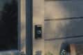 Smart doorbell with a glowing blue ring mounted on a wooden exterior wall.