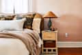 Bedroom with a beige bed, floral pillows, a woven blanket, and a wicker nightstand with a lamp.