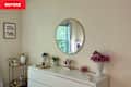 Dresser with a round mirror, pink flowers in a vase, and decorative items on a light surface.