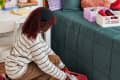 girl in dorm room crouching down placing a pink basket with shoes underneath bed