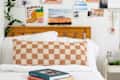 closeup shot of books on a bed with checkered orange and cream pillow behind it - photo gallery wall behind headboard
