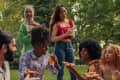 A diverse group of friends are in the community park having pizza and drinks