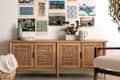 Wooden sideboard with rattan doors, decorative art prints on the wall, and a vase with greenery on top.