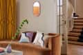 Brown velvet sofa with abstract pillows, purple vase with green plant, yellow screen, and spiral staircase in background.