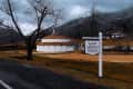 Historic Warm Springs Pools building with a sign, surrounded by bare trees and mountains under a cloudy sky.
