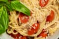 bowl of spaghetti with cherry tomatoes and basil leaves on a wooden table