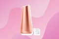 Rose gold skincare device with a small clear measuring cup on a pink abstract background.