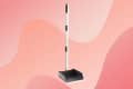 Black dustpan with a long silver handle on a pink abstract background.