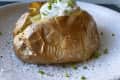 Baked potato topped with sour cream and chives on a speckled plate.