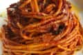 Spaghetti with rich tomato sauce, garnished with black pepper and olive oil on a white plate.