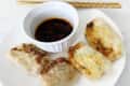 Four crispy dumplings on a white plate with a small bowl of soy sauce and chopsticks.