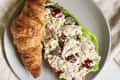 Croissant filled with chicken salad, grapes, and lettuce on a gray plate.