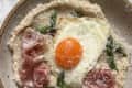 Fried sunnyside up egg over cooked oat bran with prosciutto and asparagus